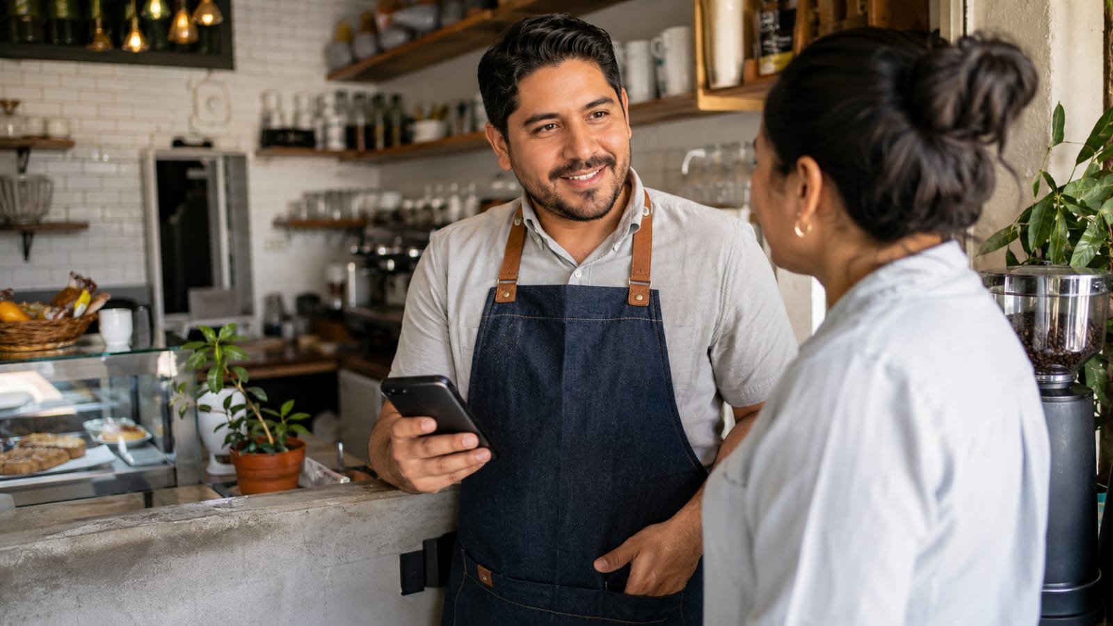 Dueño de negocio local atendiendo en su cafetería con un celular